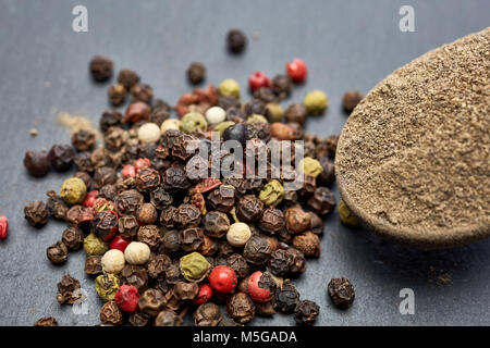 Vue de dessus d'une cuillère en bois plein de grind poudre de poivre noir entouré de noir, blanc, jaune et rouge piment isolé sur fond gris, shallo Banque D'Images