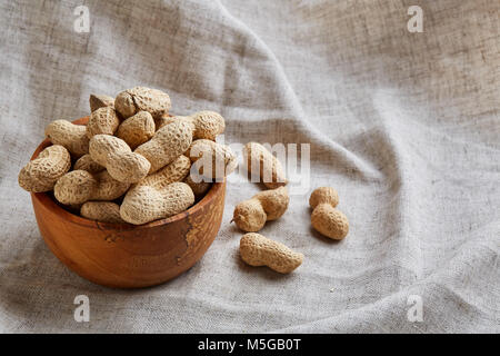 Composition de matières non épluché d'arachides à bol en bois gris clair sur le coton, nappe ou une serviette, une copie de l'espace, gros plan, selective focus. Vie saine Banque D'Images