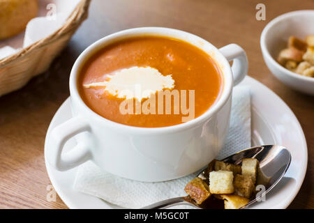 Soupe de tomates avec de la crème et des craquelins dans une assiette blanche sur la table Banque D'Images