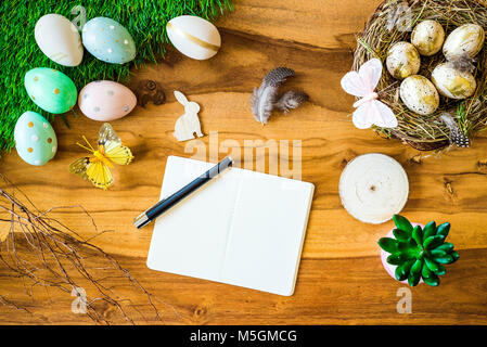 Joyeuses Pâques en plongée des comme flatlay avec carnet et un stylo pour le message et rétro coloré des œufs de Pâques, de l'herbe, papillon et nid de Pâques sur wo Banque D'Images