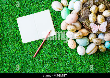 Joyeuses Pâques en plongée des comme flatlay avec ordinateur portable en blanc pour le message et les oeufs de Pâques colorés retro, herbe, papillon et nid de Pâques Banque D'Images