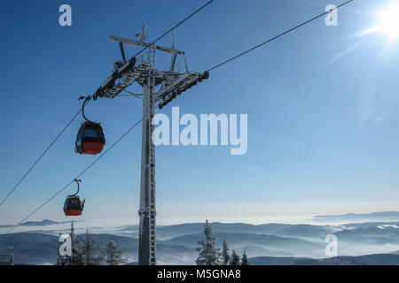 Cabine téléphérique Télécabine dans la station de ski au-dessus de la forêt en arrière-plan de montagnes enneigées en journée ensoleillée avec copie espace. Banque D'Images