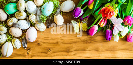 Joyeuses Pâques en plongée des comme flatlay avec bannière rétro coloré des œufs de pâques, papillon et de tulipes colorées sur table en bois Banque D'Images