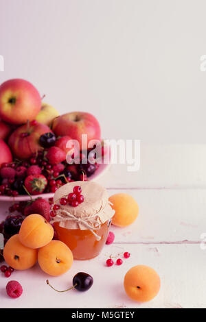 Confiture d'abricot sur un fond de fruits et petits fruits (abricots, pommes, fraises, framboises, groseilles, cerises). Banque D'Images