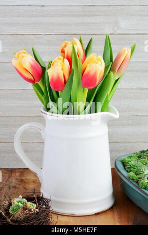 Tulipes rouges et jaunes en vintage verseuse à fond de bois. Format vertical et tourné en lumière naturelle. Banque D'Images