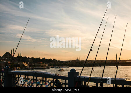 Photo conceptuelle. Des cannes à pêche sur le pont de Galata à Istanbul contre le coucher du soleil. La pêche est un passe-temps populaire parmi les habitants de la ville Banque D'Images