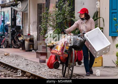 Une vendeuse de fruits pousse sa bicyclette contenant des fruits le long de 'train Street' à Hanoi, Vietnam. Les gens vivent dans cette rue malgré les trains qui détonnent à grande vitesse plusieurs fois par jour Banque D'Images