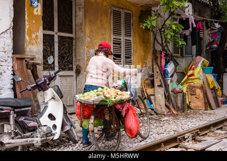 Une vendeuse de fruits pousse sa bicyclette contenant des fruits le long de 'train Street' à Hanoi, Vietnam. Les gens vivent dans cette rue malgré les trains qui détonnent à grande vitesse plusieurs fois par jour Banque D'Images