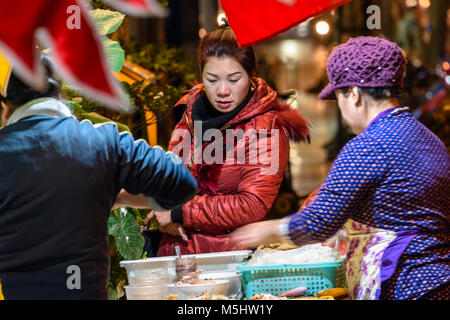 Une femme regarde un fournisseur d'aliments de rue cuit les aliments sur son stand portable, Hanoi, Vietnam. Banque D'Images