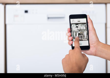 Close-up of Woman's Hand montrant lave-vaisselle App On Mobile Phone In Kitchen Banque D'Images