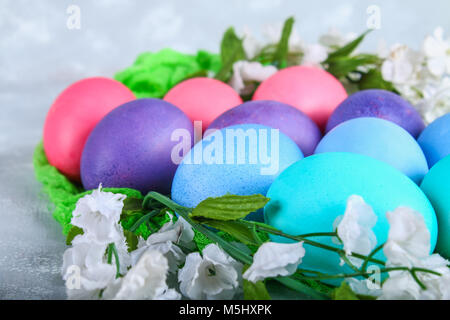 Œufs de Pâques colorés avec des fleurs blanches sur un fond de béton gris Banque D'Images