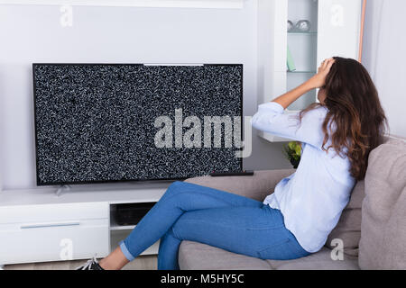 Vue arrière d'une femme sur canapé obtenir frustré avec Glitch écran de télévision à la maison Banque D'Images