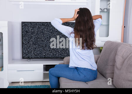 Vue arrière d'une femme sur canapé obtenir frustré avec Glitch écran de télévision à la maison Banque D'Images