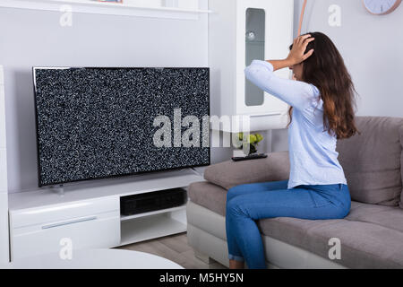 Vue arrière d'une femme sur canapé obtenir frustré avec Glitch écran de télévision à la maison Banque D'Images