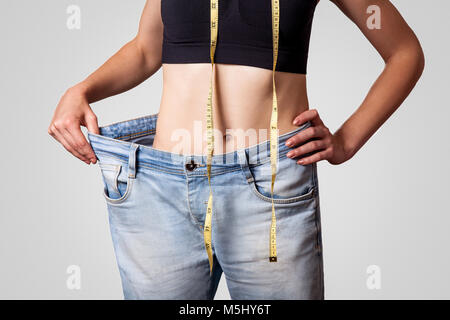 Close-up de taille fine de jeune femme en gros jeans montrant la perte réussie de poids, isolé sur fond gris clair, le régime alimentaire concept. Banque D'Images