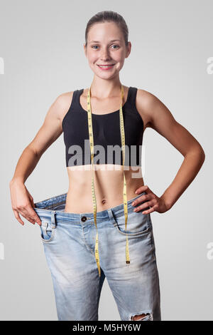 Close-up de taille fine de jeune femme en gros jeans montrant la perte réussie de poids, isolé sur fond gris clair, le régime alimentaire concept. Banque D'Images