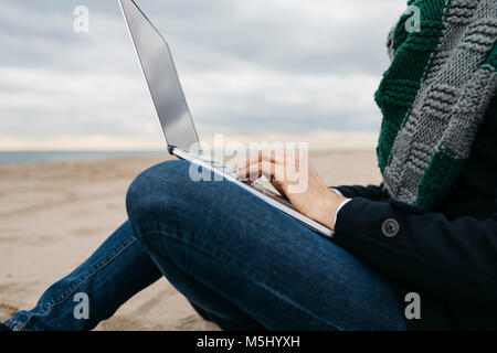 Portrait sur la plage en hiver à l'aide d'un ordinateur portable, vue partielle Banque D'Images