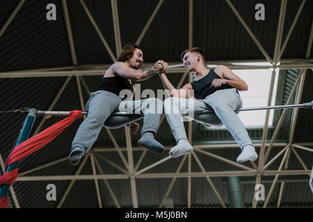 Deux gymnastes souriant assis sur high bar shaking hands in gym Banque D'Images