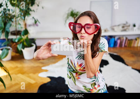 Jeune femme à lunettes en forme de cœur en tenant selfies Banque D'Images