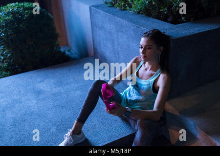 Jeune femme avec un casque rose assis sur le sol en milieu urbain moderne dans la nuit Banque D'Images