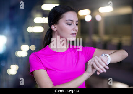 Jeune femme en rose sportshirt contrôler sa smartwatch Banque D'Images
