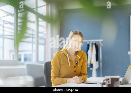 Portrait of smiling Fashion designer sitting at desk in her Studio Banque D'Images