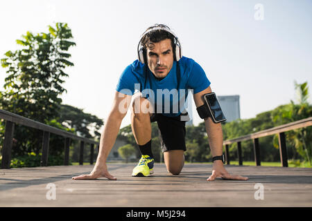 Position de départ de la formation de canaux chauds sur rue en parc urbain, portant des écouteurs Banque D'Images