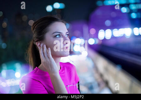 Jeune femme en rose sportshirt en écoutant de la musique en ville la nuit Banque D'Images
