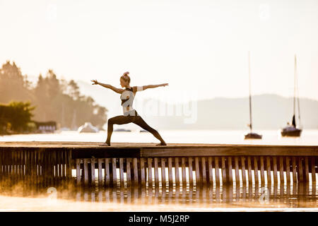 Woman practicing yoga on jetty at un lac Banque D'Images