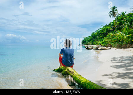 Panama, Bocas del Toro, Cayo Zapatilla, homme assis sur tronc d'arbre sur la plage Banque D'Images
