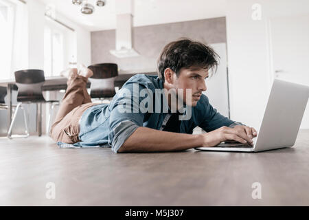 Homme étendu sur le sol dans un loft using laptop Banque D'Images