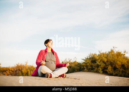 Pregnant woman practicing yoga sur la plage en hiver Banque D'Images