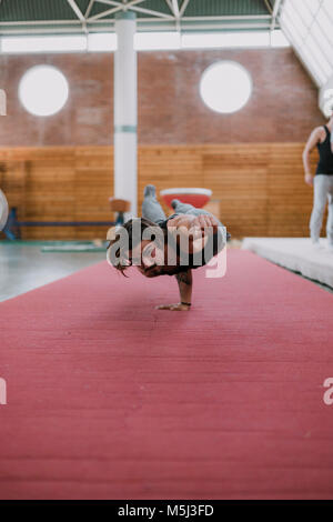 Jeune homme faisant l'exercice acrobatique in gym Banque D'Images