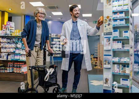 Pharmacien et souriant avec la clientèle en pharmacie walker à roues Banque D'Images