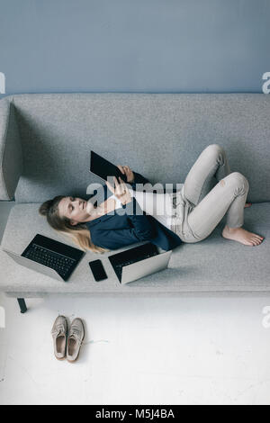 Businesswoman couché sur la table avec plusieurs appareils électroniques à l'aide de tablet Banque D'Images