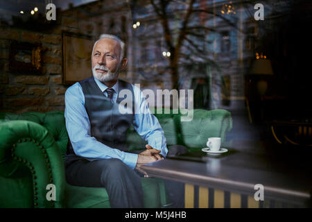 Élégant senior man sitting on couch in a cafe à la fenêtre de Banque D'Images