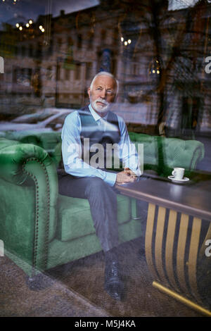 Élégant senior man sitting on couch in a cafe à la fenêtre de Banque D'Images