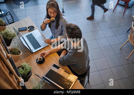 Jeune femme et l'homme dans un café avec des ordinateurs portables de parler et de boire l'expresso Banque D'Images