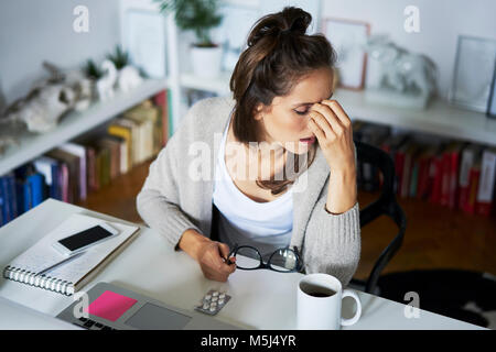 Jeune femme à la maison au bureau souffrant des maux Banque D'Images