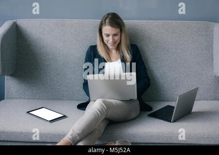 Smiling businesswoman sitting on the couch using laptop Banque D'Images