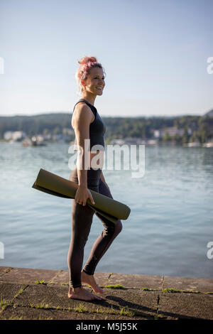 Woman in sportswear marcher avec un tapis de yoga au Lakeshore Banque D'Images