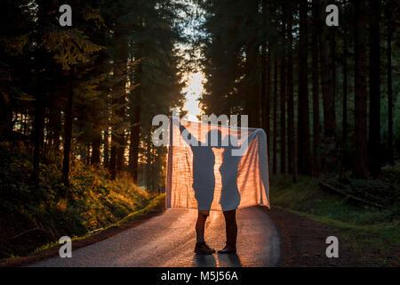 Silhouette of woman kissing couverture on country road in forest Banque D'Images