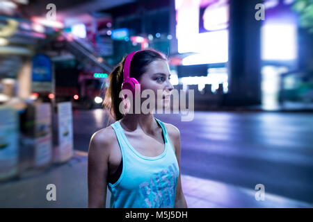 Jeune femme en rose sportshirt en milieu urbain moderne dans la nuit Banque D'Images