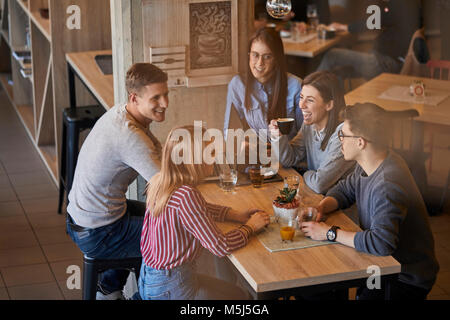 Groupe d'amis heureux assis ensemble dans un café avec un ordinateur portable et des boissons Banque D'Images