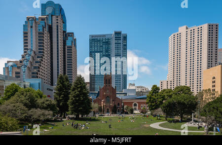 Les personnes bénéficiant de l'été soleil à Yerba Buena Gardens, San Francisco. L'église gothique St Patrick's se trouve sous l'ombre de l'édifices modernes. Banque D'Images