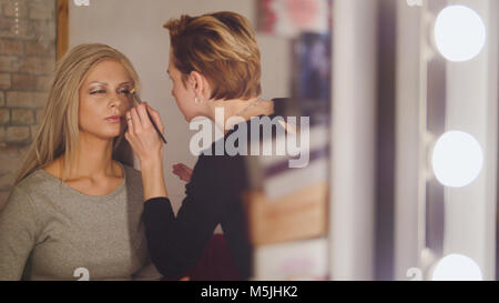 Visage - maquillage et artiste Blonde modèle près de miroir dans le dressing Banque D'Images