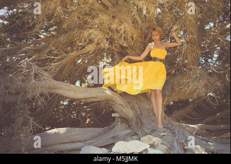 Belle jeune fille en robe jaune avec arbre puissant Banque D'Images