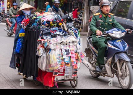 Une Vietnamienne portant un chapeau de bambou et masque de visage, pousse une charrette pleine d'articles de maison à vendre à Hanoi, Vietnam. Banque D'Images