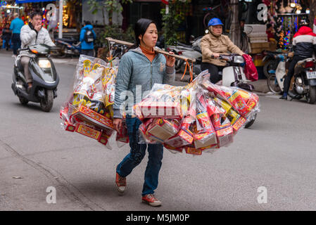 Une Vietnamienne comporte un pôle comptable bambou plein d'articles en vente pour célébrer le Nouvel An chinois à Hanoi, Vietnam. Banque D'Images