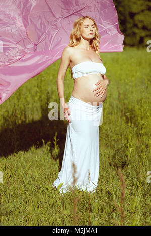 Belle femme enceinte debout dans l'herbe. Elle ferma les yeux Banque D'Images